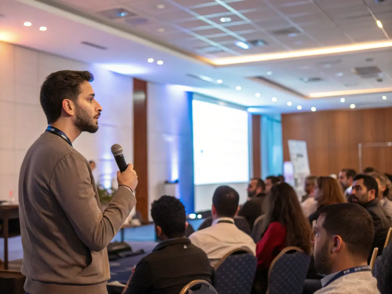 A photograph of a seminar session with a speaker presenting on stage, discussing advanced grooming techniques to a seated audience.